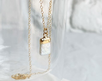 May include: A gold chain necklace with a white pearl pendant. The pendant is rectangular and has a gold frame.