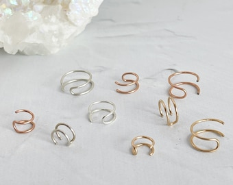 May include: A collection of seven silver, gold, and rose gold double hoop earrings. The earrings are arranged on a white surface.