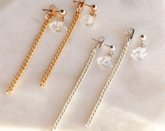 May include: Two pairs of dangle earrings with a clear crystal charm hanging from a delicate chain. One pair has a gold chain and the other has a silver chain.