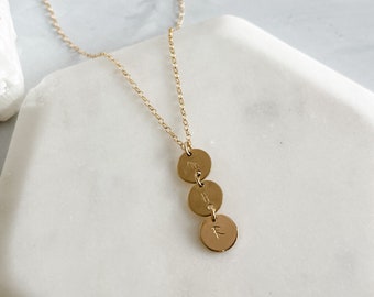 May include: A gold chain necklace with three gold discs hanging from it. Each disc has a letter engraved on it: "M", "H", and "F".