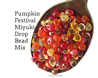 May include: A spoon filled with a mix of red, orange, and yellow glass beads. The beads are small and have a teardrop shape. The text "Pumpkin Festival Miyuki Drop Bead Mix" is written above the spoon.
