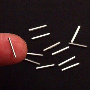 Pu&ograve; includere: Primo piano di un mucchio di aste metalliche argentate su una superficie nera. Le aste sono lunghe circa 2,5 cm e sono disposte in modo casuale.