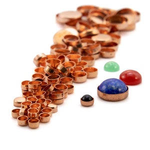 May include: A large pile of copper-colored metal cup-shaped settings with a variety of colorful cabochon gemstones, including green, red, blue, and black.