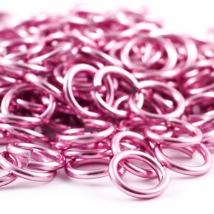 May include: A close-up of a pile of pink metal jump rings. The rings are small and round, and they are all linked together.