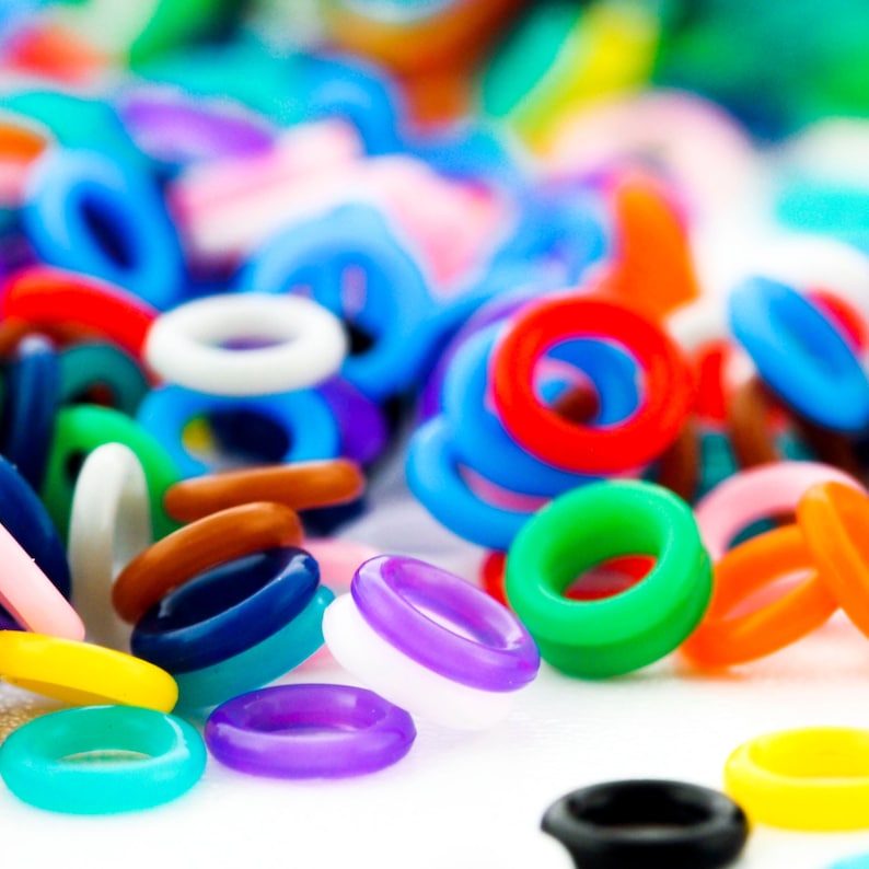 K&ouml;nnte beinhalten: Eine Sammlung bunter Plastikringe in verschiedenen Gr&ouml;&szlig;en und Formen. Die Ringe liegen auf einer wei&szlig;en Oberfl&auml;che.