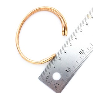 K&ouml;nnte beinhalten: Ein goldfarbenes Armreif-Armband, das mit einem Lineal gemessen wird und einen Durchmesser von etwa 15 cm hat.