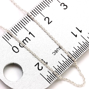 May include: A silver chain necklace measuring 2 inches in length, laid out on a ruler with markings in centimeters.