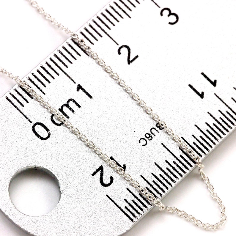 May include: A silver chain necklace measuring 2 inches in length, laid out on a ruler with markings in centimeters.