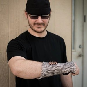 May include: A person wearing a black t-shirt and a black cap with a silver chainmail bracelet with copper accents on their wrist.