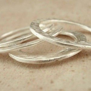May include: Four silver rings stacked on top of each other. The rings are all smooth and have a hammered texture.
