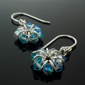 Könnte beinhalten: Ein Paar silberne Ohrringe mit blauen und klaren Kristall-Akzenten. Die Kristalle sind in Blütenform angeordnet und werden von silbernem Draht zusammengehalten.