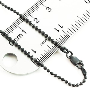 May include: A black ball chain necklace with a lobster clasp. The chain is measured against a ruler, showing it is 17 inches long.