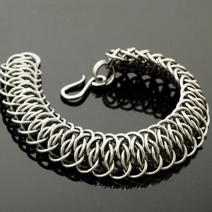 May include: A silver chain bracelet with a unique interlocking design. The bracelet is made of small, round links that are woven together to create a strong and durable piece of jewelry.