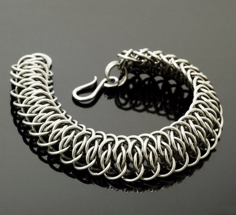May include: A silver chain bracelet with a unique interlocking design. The bracelet is made of small, round links that are woven together to create a strong and durable piece of jewelry.