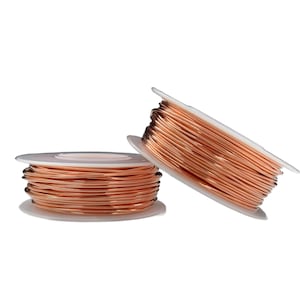May include: Two spools of shiny copper-coloured wire wound tightly around white plastic circular cores. The wire has a smooth, metallic finish and is coiled in multiple layers, creating a cylindrical shape on each spool. The spools are positioned side by side.