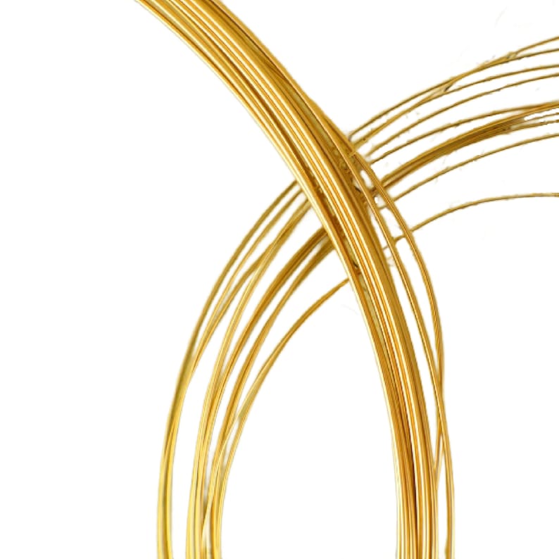 May include: A collection of thin, flexible gold-colored metal wires arranged in overlapping circular loops. The metallic strands feature a smooth, reflective surface that catches the light, creating a series of curved lines against a plain white background.