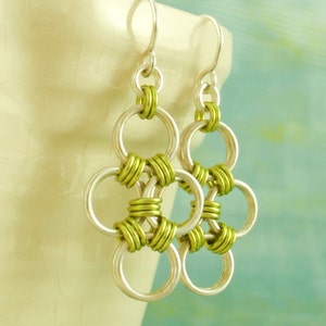 May include: Silver earrings with a green chainmail design. The earrings are made of metal and have a dangling design.