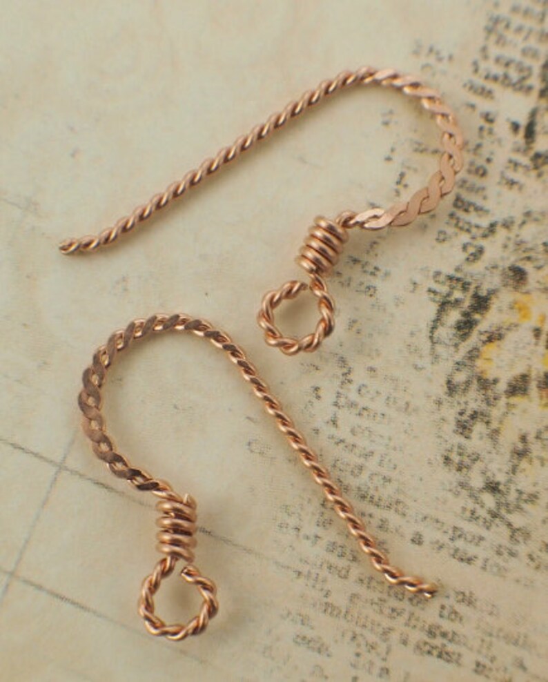 May include: Two copper-colored earring hooks. Each hook features a twisted wire design for the main body, transitioning to a flattened, braided section at the top. The bottom of each hook has a small, coiled loop.
