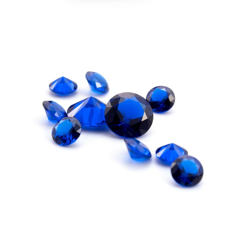May include: A group of blue gemstone crystals scattered on a white background. The crystals are faceted and have a brilliant shine.