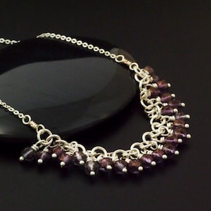 Peut inclure: Un collier en chaîne argent avec une rangée de perles de verre violettes foncées en cascade.