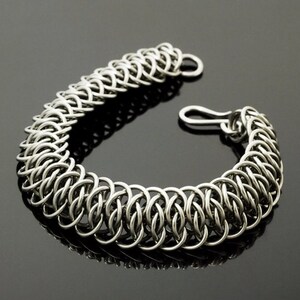 May include: A silver chainmail bracelet with a clasp closure. The bracelet is made of interlocking metal rings.