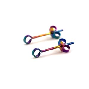 Könnte beinhalten: Ein Paar Regenbogen-Titan-Ohrringe mit einer kleinen Schlaufe am Ende jedes Stiftes.