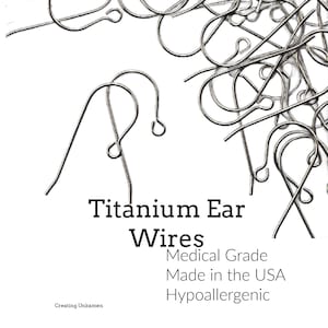 May include: A collection of silver-toned titanium ear wires for jewelry making. The text reads: Titanium Ear Wires, Medical Grade, Made in the USA, Hypoallergenic, Creating Unkamen. These curved metal hooks feature a small loop at the bottom.