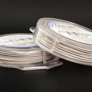 Peut inclure: Deux bobines de fil Artistic Wire plaqué argent, chacune dans un récipient en plastique transparent. Le fil est blanc et les bobines sont étiquetées avec le nom de la marque et la taille.