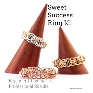 Peut inclure: Trois anneaux en maille sur des supports en bois. Les anneaux sont en métal de couleur argent, or et cuivre. Le texte "Sweet Success Ring Kit" est en haut de l'image. Le texte "Beginner Chainmaille Professional Results" est en bas de l'image.