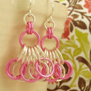 May include: Pink and silver dangle earrings with multiple interconnected rings. The earrings are made of metal and have a delicate, feminine design.