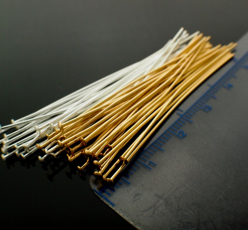 May include: Close-up of a collection of head pins in gold and silver tones. The pins are arranged in a neat pile, with a ruler in the background. The pins are used for jewelry making and crafting.