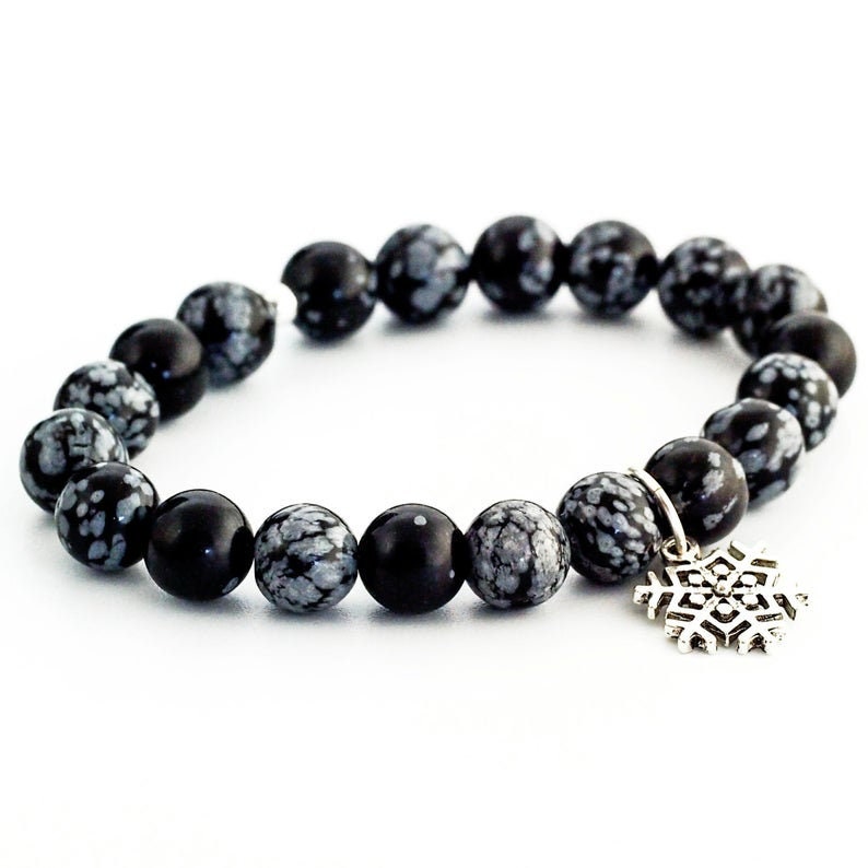 Puede incluir: Pulsera de cuentas de obsidiana negra y blanca con un dije de copo de nieve plateado.