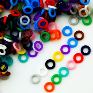 K&ouml;nnte beinhalten: Eine Sammlung bunter Gummringe in verschiedenen Gr&ouml;&szlig;en. Die Ringe sind in einem Haufen und einer Linie angeordnet und zeigen einen Regenbogen an Farben.