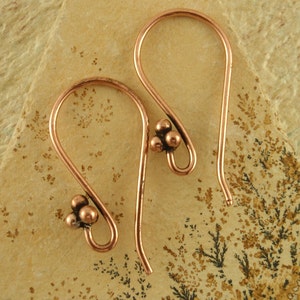 May include: A pair of copper hoop earrings with a cluster of three small copper beads on each earring.