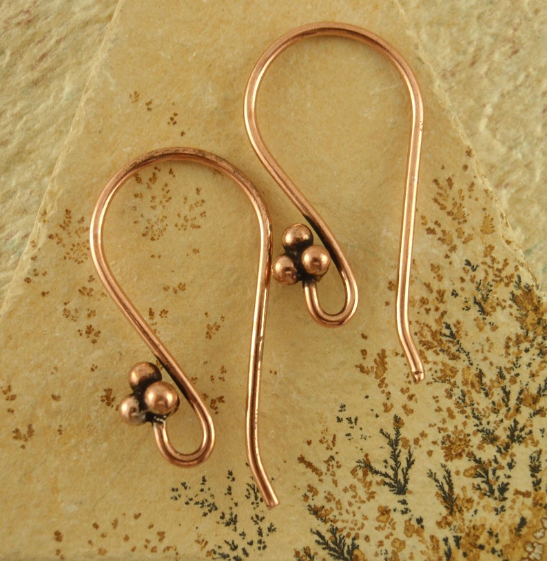 May include: A pair of copper hoop earrings with a cluster of three small copper beads on each earring.