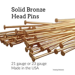 Puede incluir: Una colecci&oacute;n de alfileres de cabeza de bronce met&aacute;lico con cabezas circulares planas. El texto en la imagen dice: Solid Bronze Head Pins, 21 gauge or 23 gauge, Made in the USA y Creating Unkamen. Los alfileres est&aacute;n en un grupo denso.