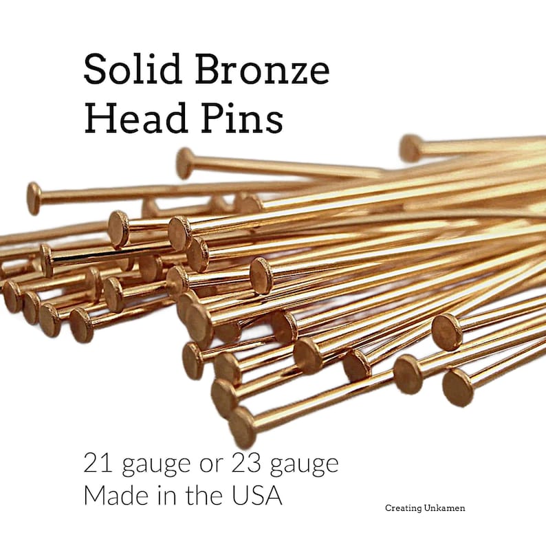Puede incluir: Una colecci&oacute;n de alfileres de cabeza de bronce met&aacute;lico con cabezas circulares planas. El texto en la imagen dice: Solid Bronze Head Pins, 21 gauge or 23 gauge, Made in the USA y Creating Unkamen. Los alfileres est&aacute;n en un grupo denso.