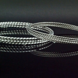 May include: Two silver-toned metal bracelets featuring a twisted, rope-like texture. The bracelets are circular in shape and have a matte, metallic finish. They are positioned to overlap slightly, creating a reflective appearance on the surface.