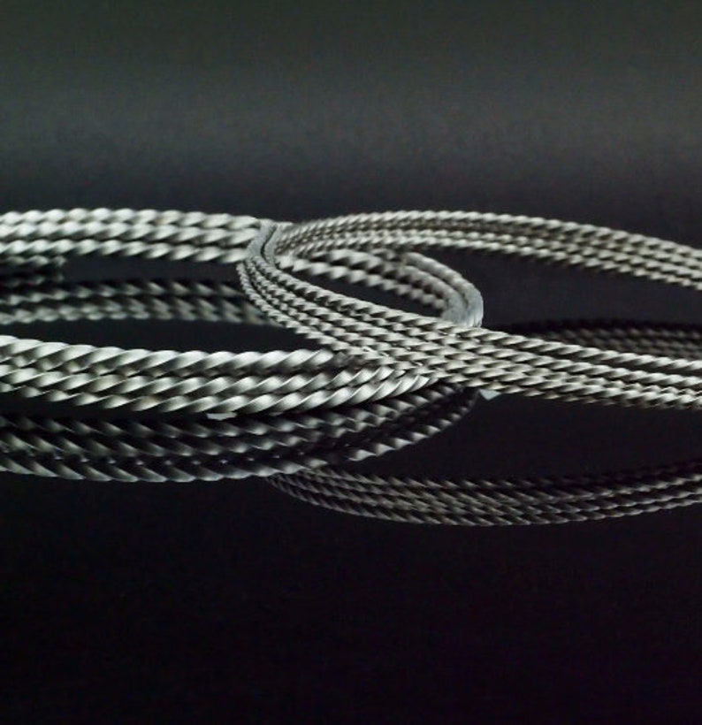May include: Two silver-toned metal bracelets featuring a twisted, rope-like texture. The bracelets are circular in shape and have a matte, metallic finish. They are positioned to overlap slightly, creating a reflective appearance on the surface.