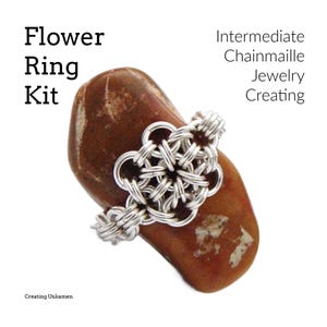 May include: A silver chainmaille flower ring kit. The ring is made with a silver chainmaille flower design and is shown on a brown stone.