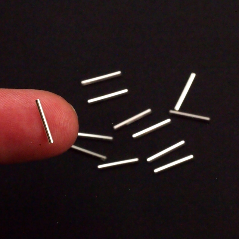 Pu&ograve; includere: Primo piano di un mucchio di aste metalliche argentate su una superficie nera. Le aste sono lunghe circa 2,5 cm e sono disposte in modo casuale.