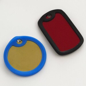 May include: Two blank dog tags, one round with a blue border and a gold center, and one rectangular with a black border and a red center.