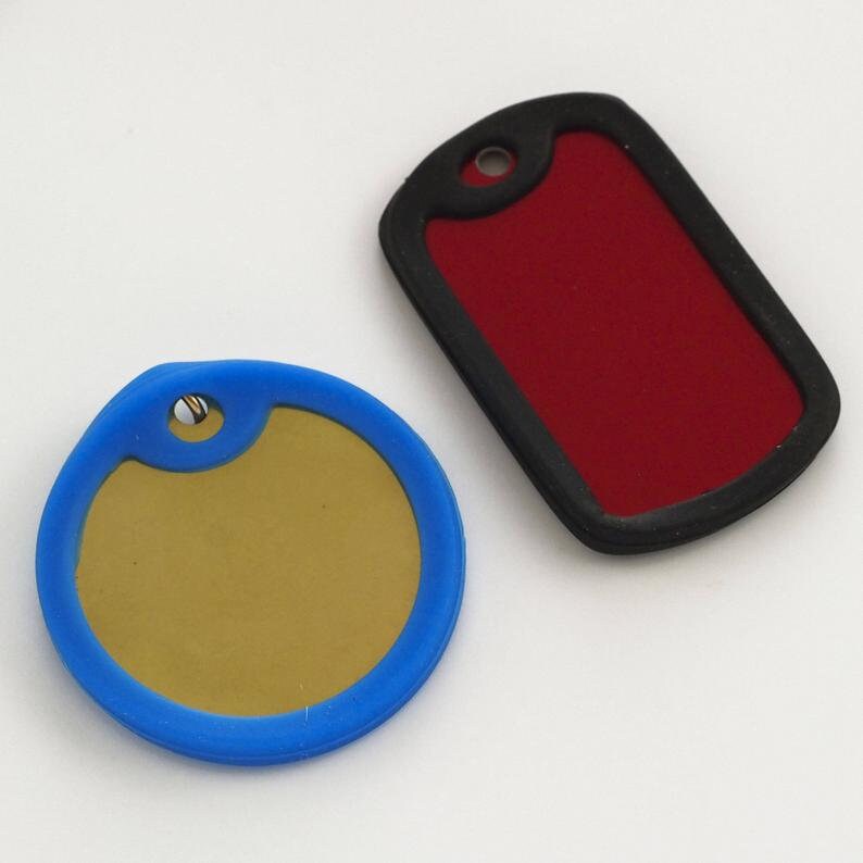 May include: Two blank dog tags, one round with a blue border and a gold center, and one rectangular with a black border and a red center.