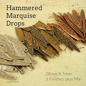 Puede incluir: Un montón de gotas de marquise de metal martillado en tres acabados: plata, cobre y latón. Las gotas miden 28 mm de largo y 5 mm de ancho. "3 Finishes plus Mix" está escrito debajo de las gotas.