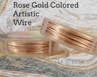 Op de afbeelding: Twee doorzichtige plastic spoelen met rosékleurige artistieke draad. De tekst op de afbeelding luidt Rose Gold Colored Artistic Wire en 14-30 gauge. De draad is strak rond het midden van elke spoel gewikkeld en heeft een metallic afwerking.