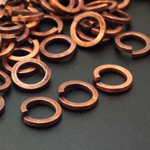 Op de afbeelding: Een verzameling koperkleurige veersluitringen. Deze cirkelvormige bevestigingsmiddelen hebben een kenmerkende opening, waardoor ze stevig vastgehouden kunnen worden. De ringen zijn verspreid, wat hun metalen glans en industriële ontwerp benadrukt.