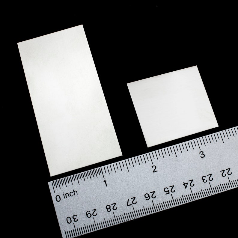 Op de afbeelding: Twee witte rechthoekige stukken papier op een zilveren liniaal met zwarte markeringen. De liniaal is gemarkeerd in inches en 1/16e inch. Het grootste stuk papier is ongeveer 1 1/2 inch lang en het kleinste ongeveer 1 inch.