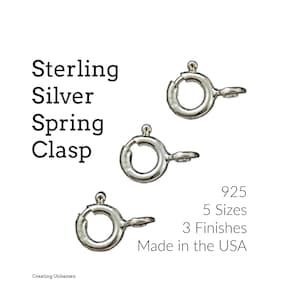Puede incluir: Tres cierres de resorte de plata, cada uno con un anillo redondo y una pequeña bola en la parte superior. El texto "925", "5 tamaños", "3 acabados" y "Hecho en los EE. UU." está impreso debajo de los cierres.
