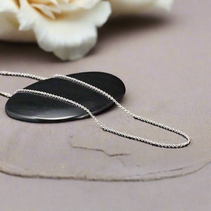 May include: A silver chain necklace on a gray surface. The chain is made of small, round links.