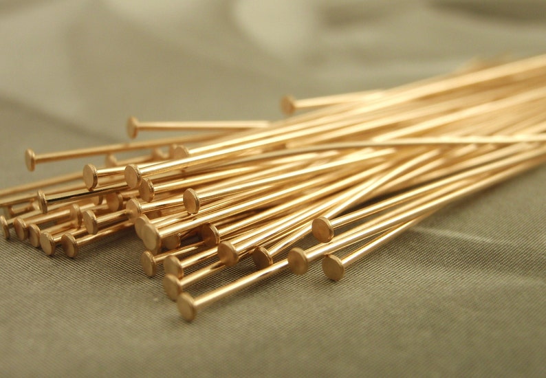 Puede incluir: Una colecci&oacute;n de numerosos alfileres de cabeza de metal en tono dorado, cada uno con un v&aacute;stago largo, delgado y recto, y una peque&ntilde;a cabeza circular plana en un extremo. Estos componentes para joyer&iacute;a est&aacute;n dispuestos en un grupo suelto.